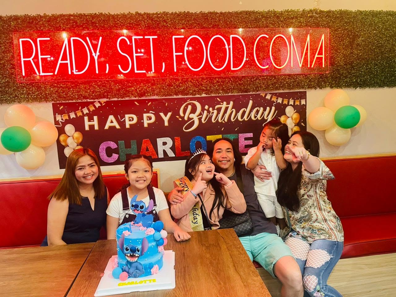 Family celebrating a birthday under the Ready, Set, Food Coma neon sign at Sweet Pepper
